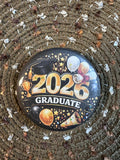 Celebrate the Class of 2026 with this bold and festive 2.25" graduation button pin. Featuring a striking gold “2026 Graduate” design with balloons, stars, and celebratory accents, this pin is perfect for graduates and supporters alike. Lightweight with a durable plastic back, it’s comfortable to wear and makes a great keepsake for graduation ceremonies, parties, and photos.